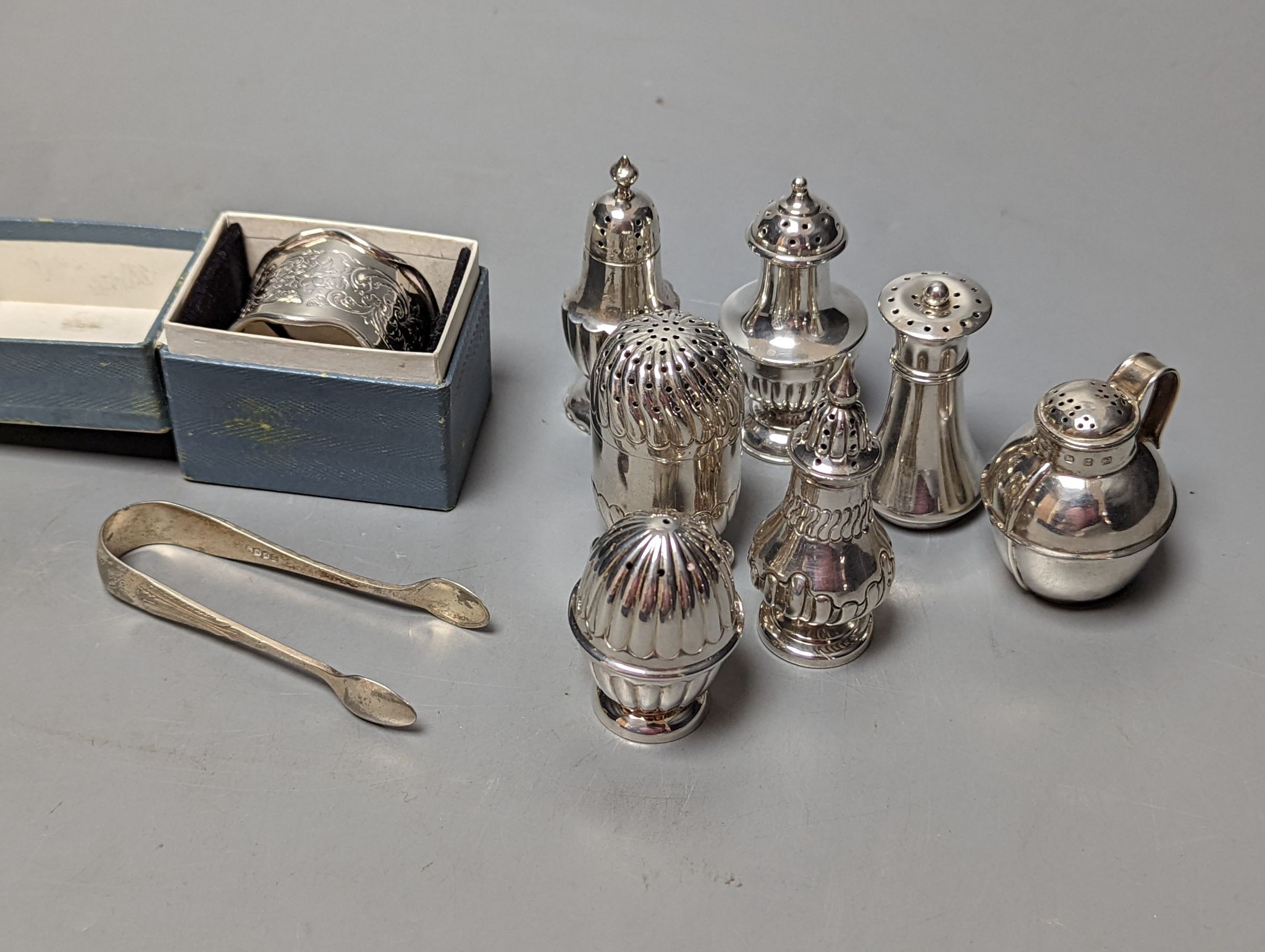 A cased silver napkin ring, seven assorted silver pepperettes including Guernsey can and a pair of plated sugar tongs.